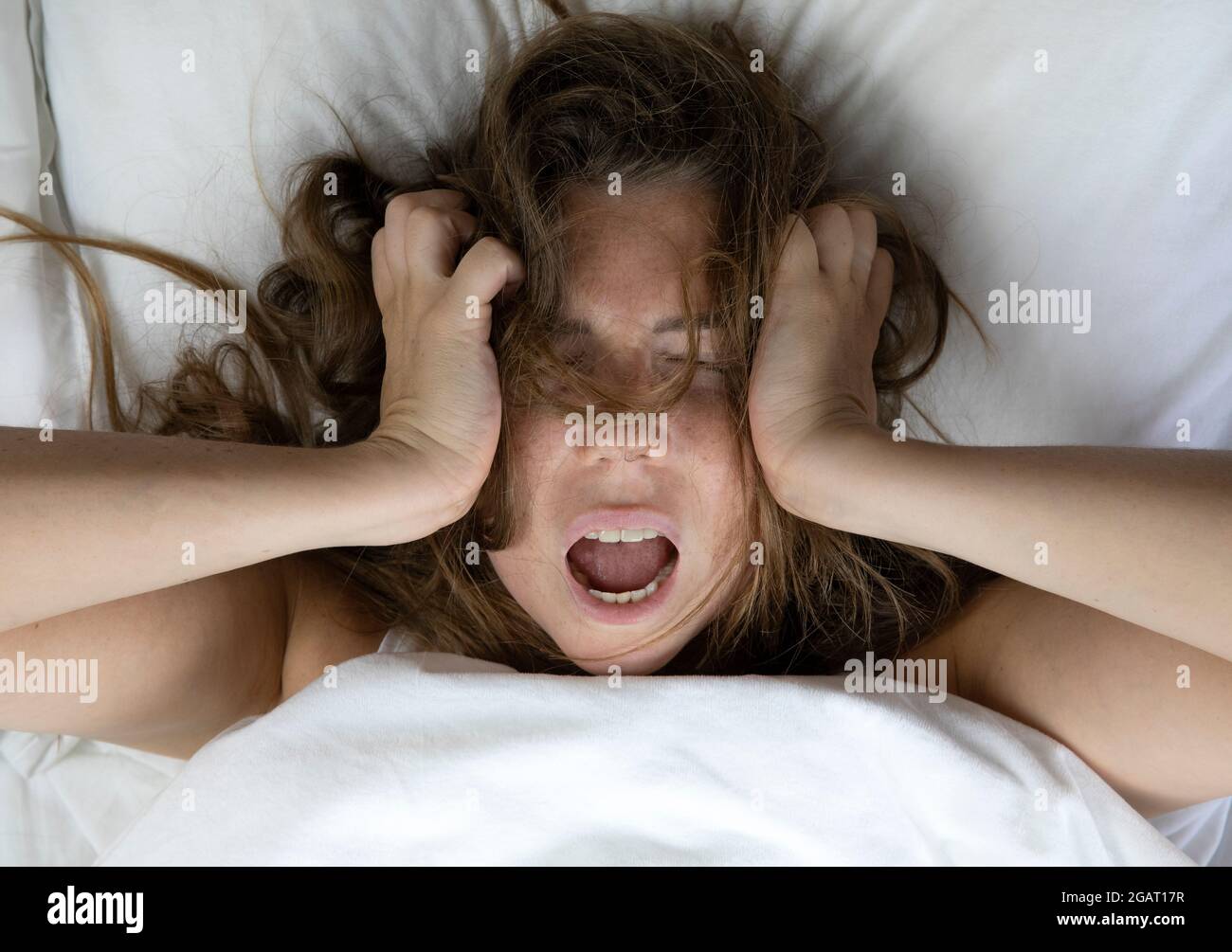Junge, depressive, unglückliche Frau, die mit gesundheitlichen Problemen im Bett liegt, schreit, kater, Depression, schlaflose Frau, Migräne von oben mit weißen Laken Stockfoto