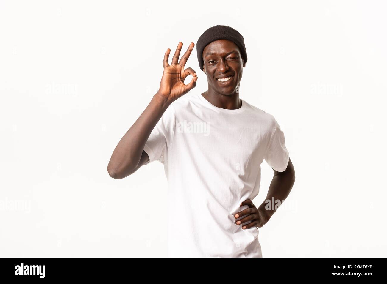 Portrait von selbstbewussten und optimistischen afroamerikanischen cool guy in Beanie, versichern alle gut, winking in Zustimmung und zeigt okay Geste, garantieren Qualität Stockfoto