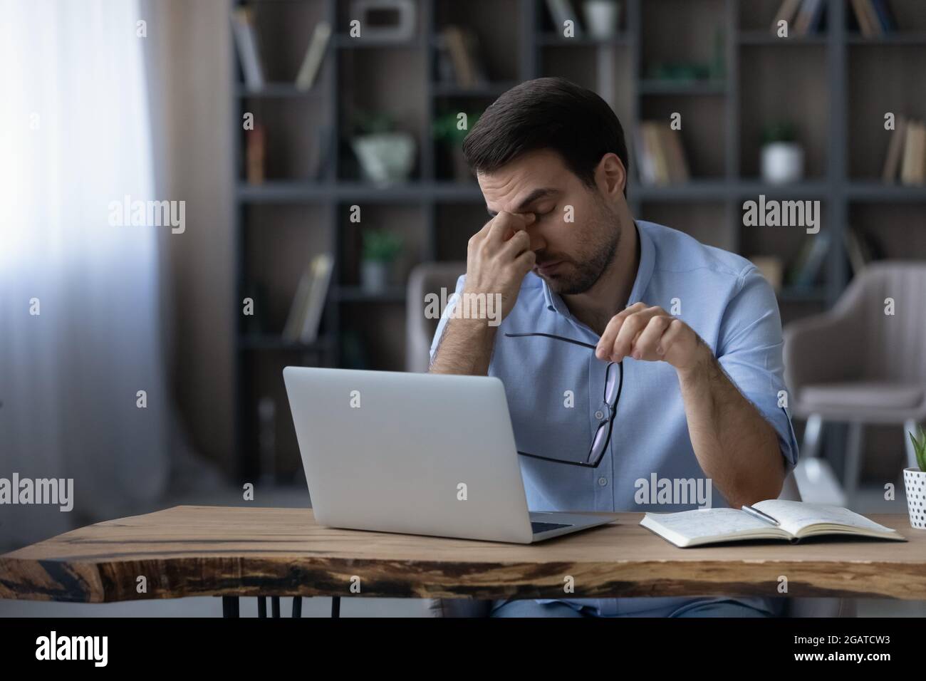 Unglücklicher Geschäftsmann aus der Millennials-Generation, der als Freiberufler tätig ist, nimmt eine Brille von der Massage-Nasenbrücke Stockfoto