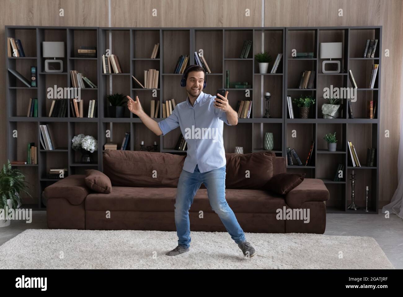 Junger Mann mit Kopfhörern tanzt im Wohnzimmer mit dem Smartphone Stockfoto