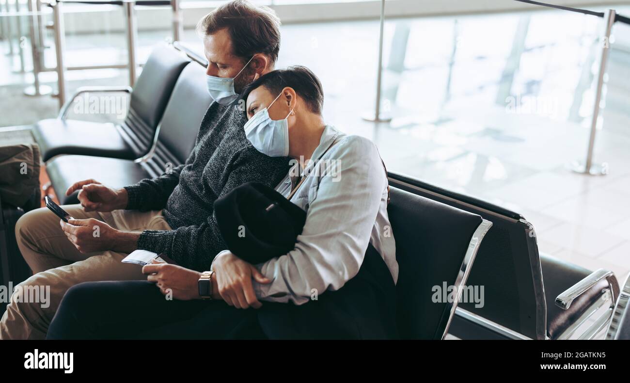 Mann und Frau, die während einer Pandemie am Flughafenterminal sitzen. Passagierpaar mit Gesichtsmasken wartet auf verspäteten Flug. Stockfoto