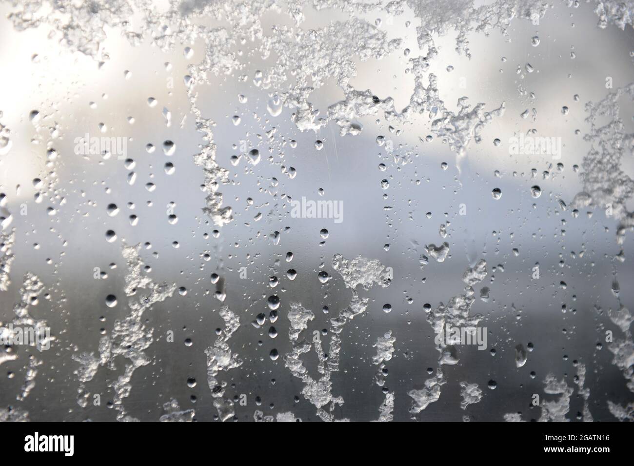Schnee, Eis und Regentropfen, die im Winter teilweise auf einer Fensterscheibe auftauen – Hintergrundbild für die Winterfunktion Stockfoto