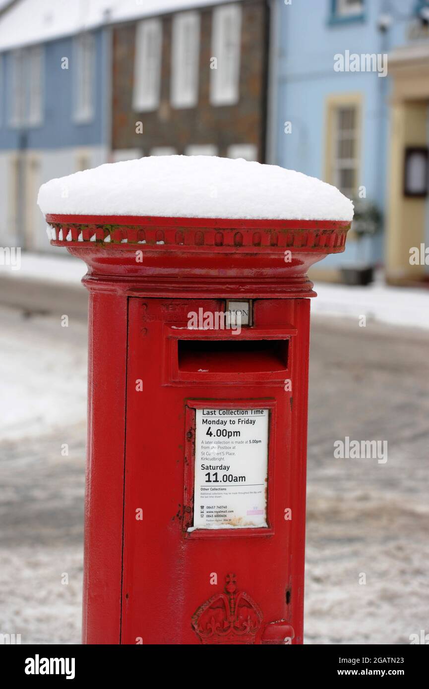 Ein leuchtend roter Briefkasten mit Winterschnee in einer Kirkcudbright Street, Schottland, Großbritannien Stockfoto