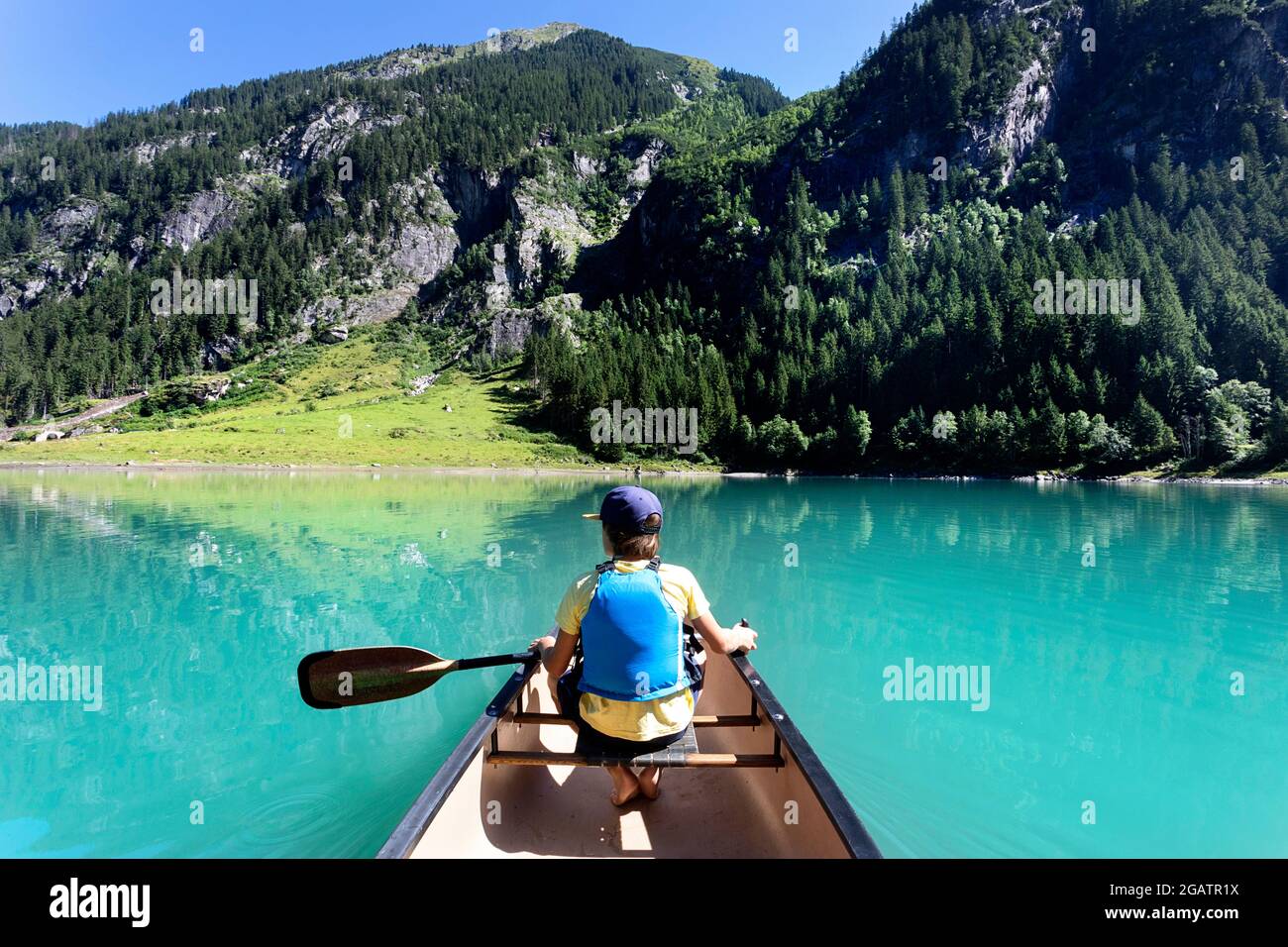 Junge sitzt im Kanu Reiten auf Bergsee in Sommer alpine Landschaft mit Wasserfall in Bacgrund. Stillup Stausee, Stillup Lake, Österreich, Tirol Stockfoto