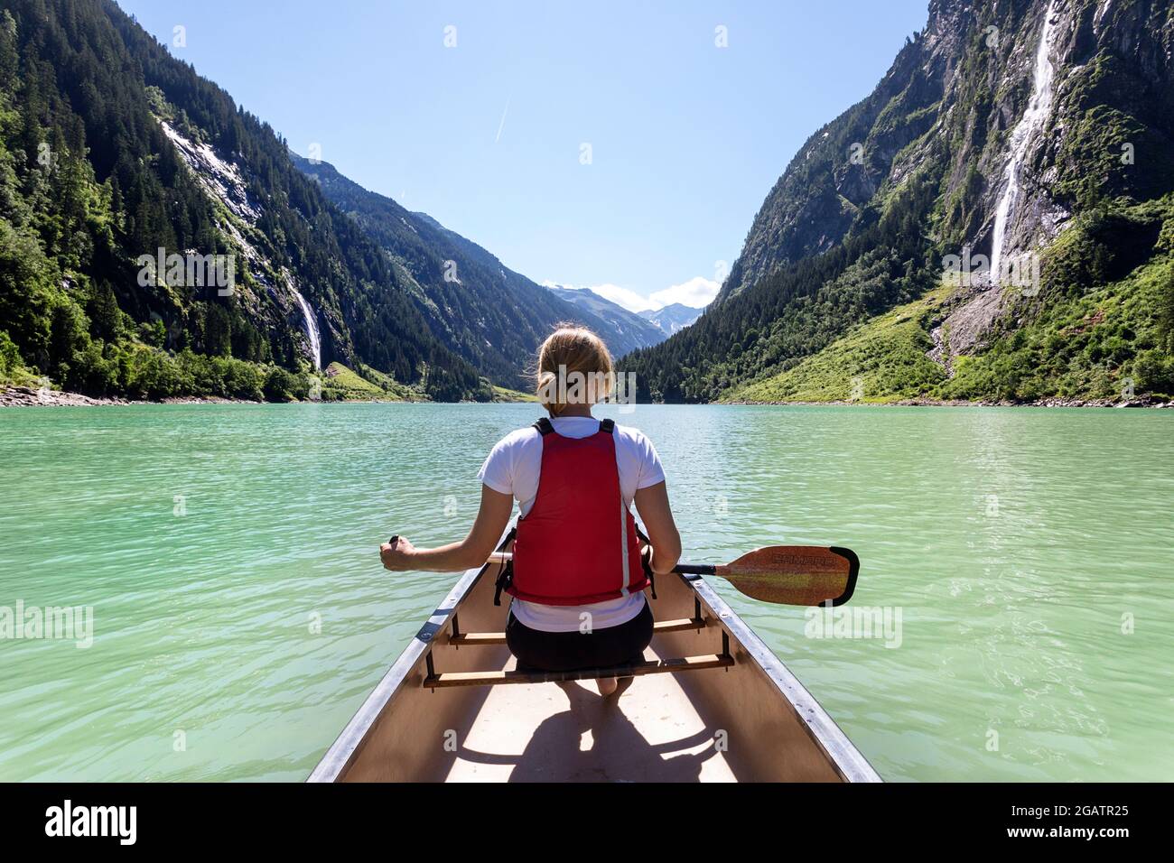 Frau sitzt im Kanu Reiten auf Bergsee im Sommer alpine Landschaft mit Wasserfällen im Hintergrund. Stillup Stausee, Stillup Lake, Österreich, Tyro Stockfoto