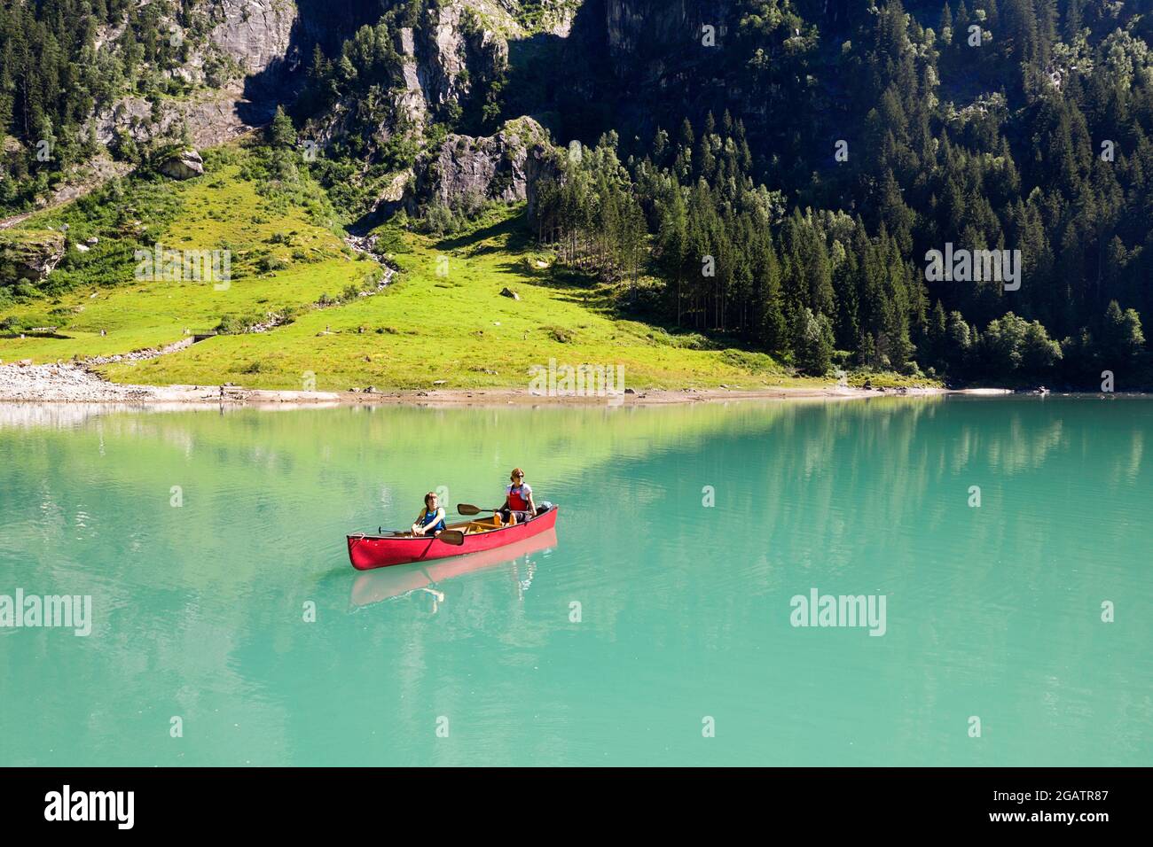 Mutter und Sohn im Kanu fahren auf Bergsee im Sommer alpine Landschaft mit Wasserfall im Hintergrund. Stillup Stausee, Stillup Lake, Österreich, Tirol Stockfoto
