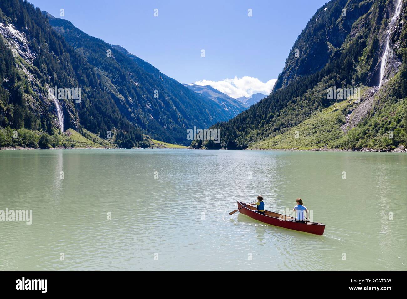 Mutter und Sohn im Kanu fahren auf Bergsee im Sommer alpine Landschaft mit Wasserfall im Hintergrund. Stillup Stausee, Stillup Lake, Österreich, Tirol Stockfoto