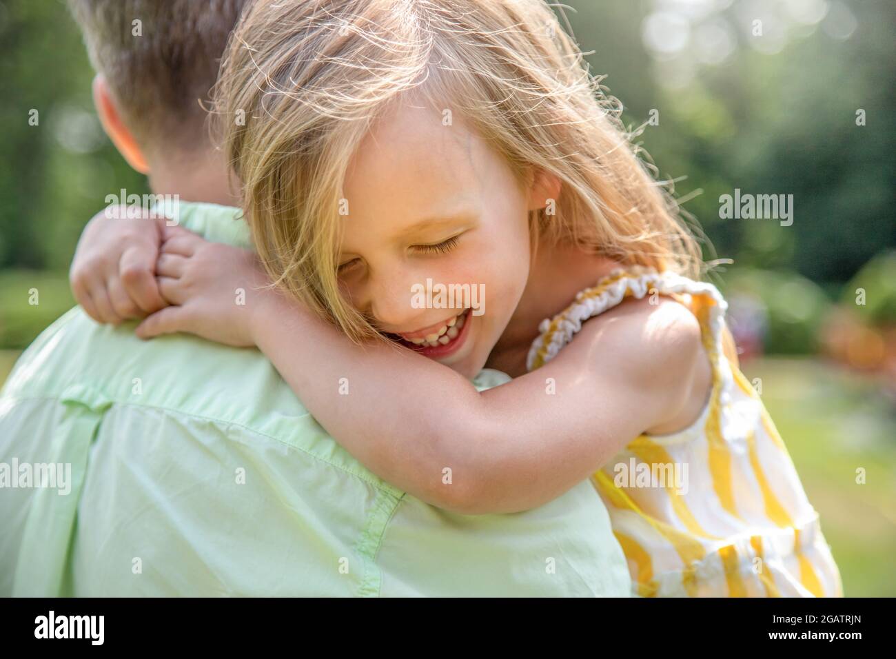 Vater hält seine Tochter in den Armen, glückliches Mädchen lacht und umarmt ihren Vater aus der Nähe. Frohe Familie Stockfoto