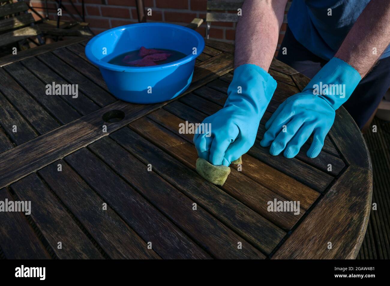 Mann mit blauen Gummihandschuhen putzt zu Beginn des Frühlings einen dunklen Gartentisch aus Holz, Kopierraum, ausgewählter Fokus Stockfoto