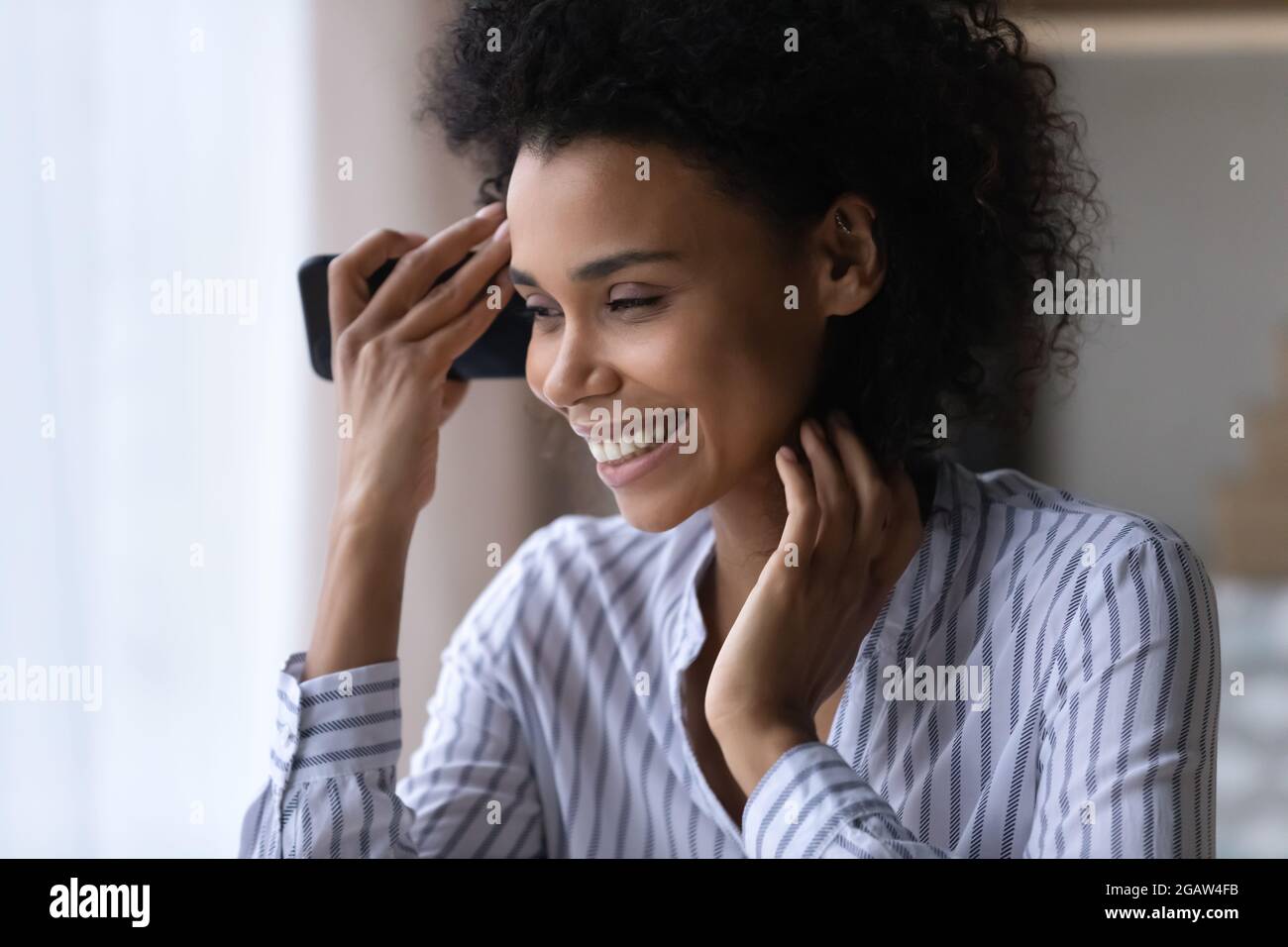 Fröhliche Mischrennerin hört sich auf dem Smartphone die Audiobotschaft an Stockfoto