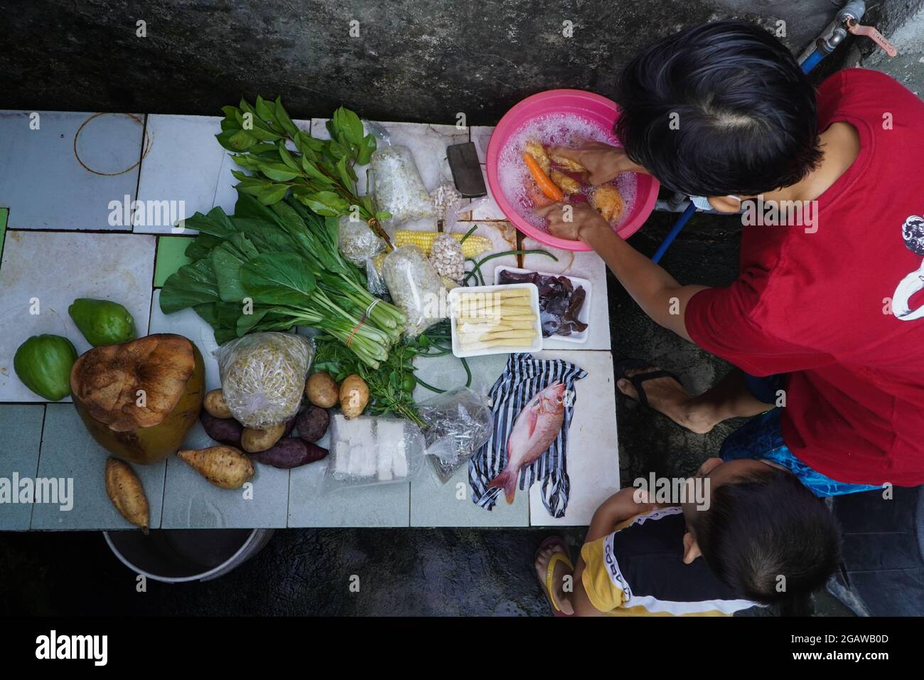 BALI, 29 2021. JULI: Eine Mutter und ihr Kleinkind waschen Gemüse, Fisch und Obst, die sie auf dem Markt gekauft haben, mit Seifenwasser. Das ist ihr Ffor Stockfoto