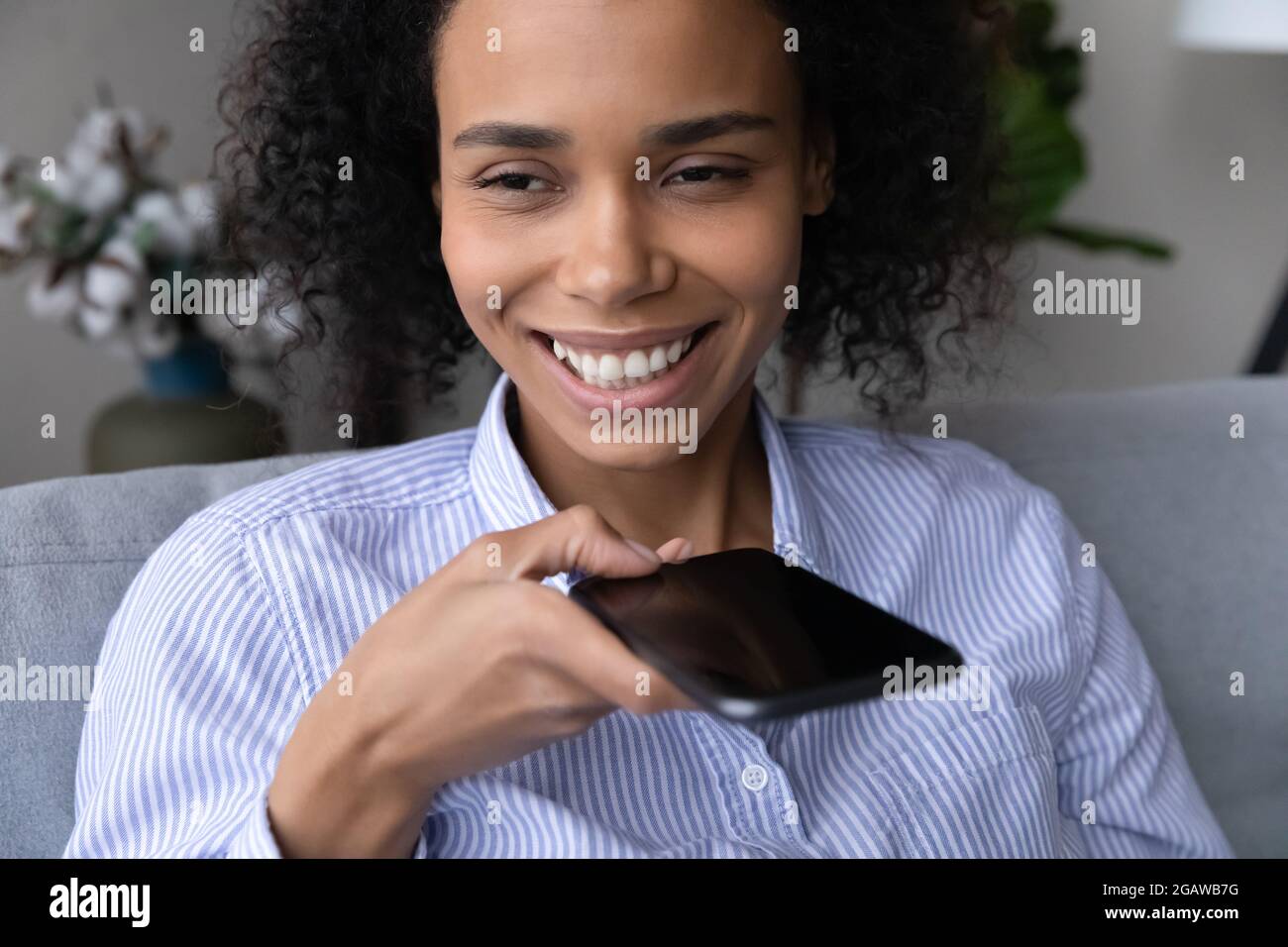 Lächelnde Birazialfrau spricht auf dem Handy über Lautsprecher Stockfoto