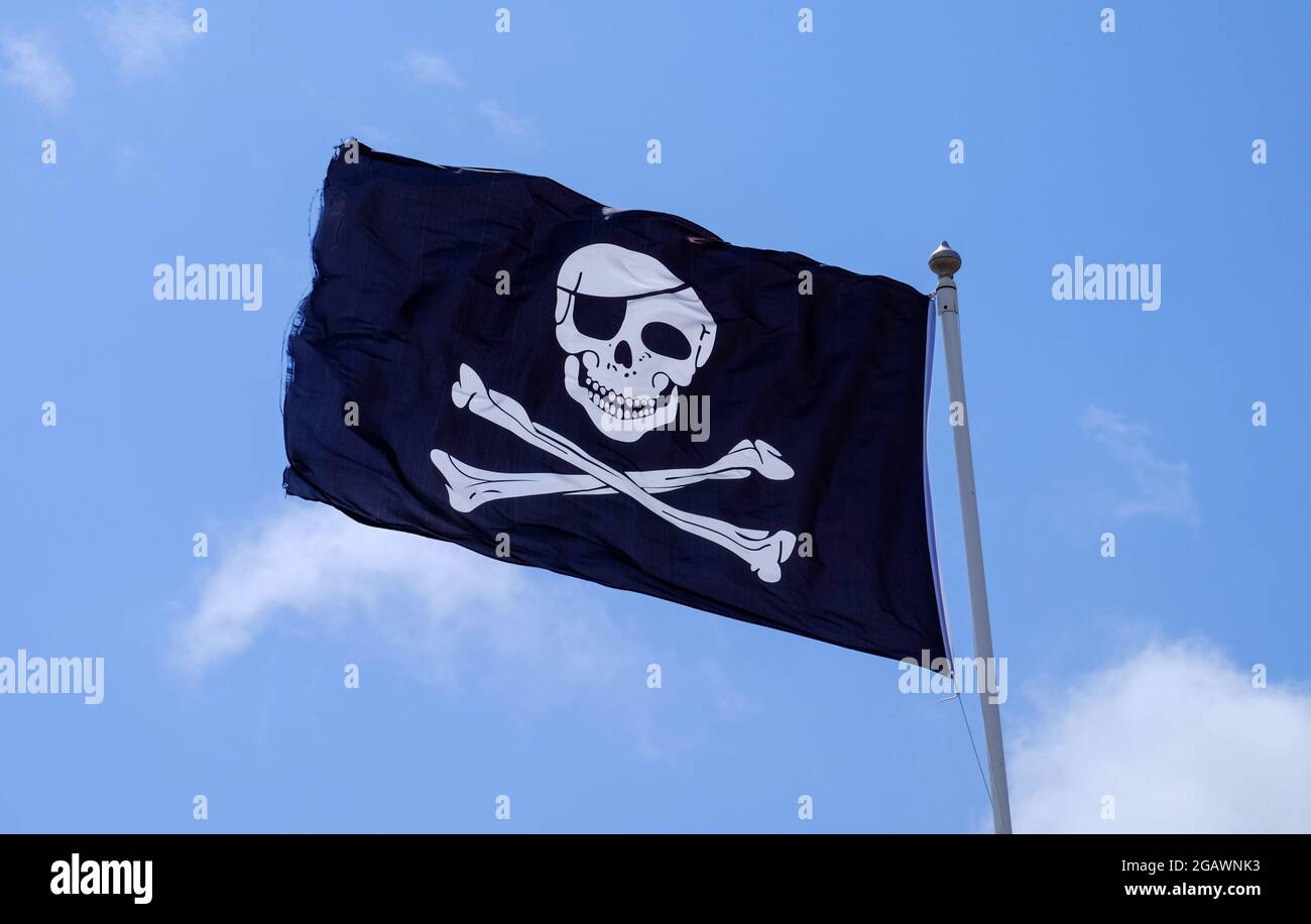 Piratenflagge, auch bekannt als Jolly Roger oder Totenkopf- und Kreuzknochen-Flagge, abgebildet vor einem blauen Himmel. Stockfoto
