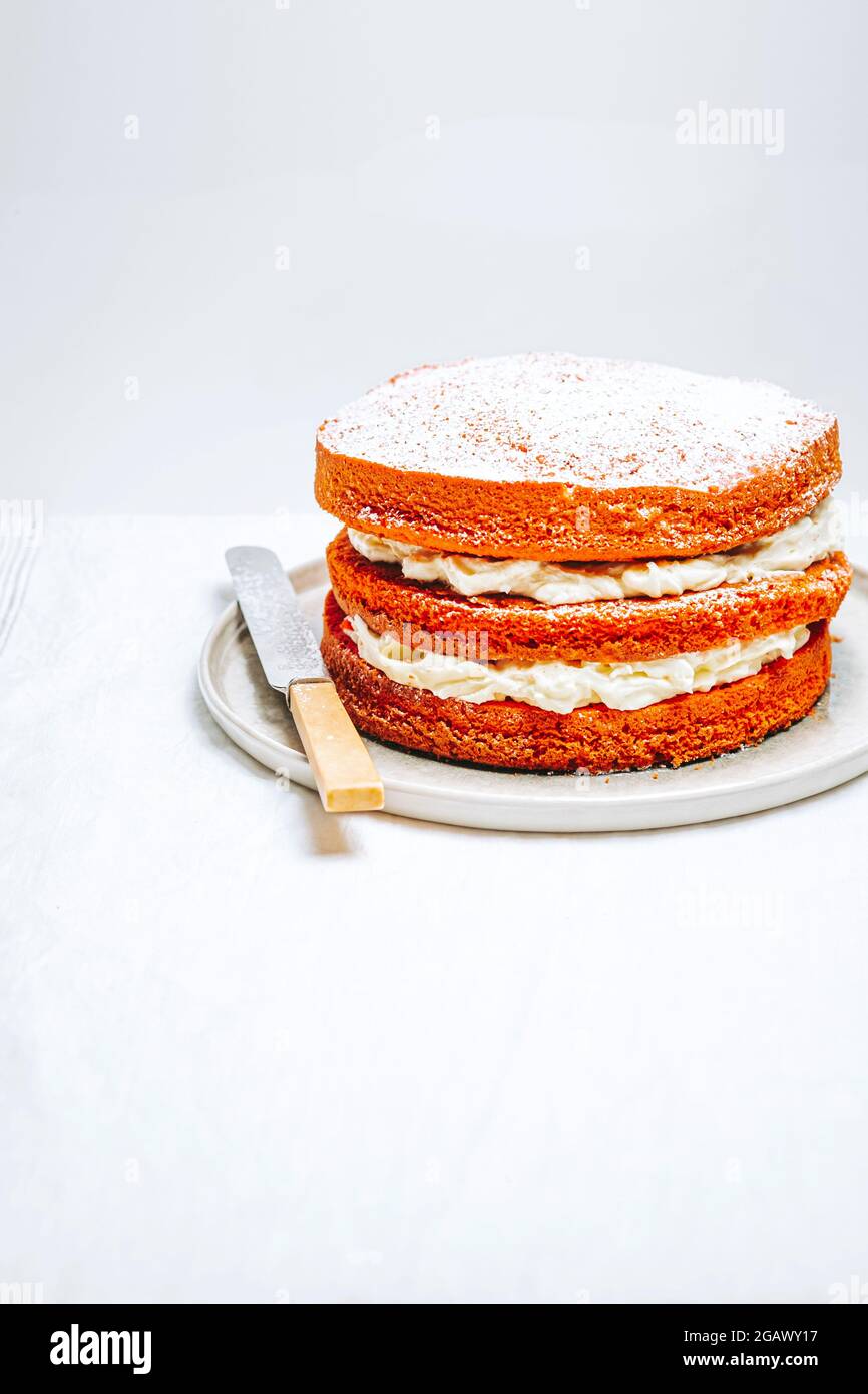 Victoria Sponge Kuchen gefüllt mit Schlagsahne auf einem Teller mit einem Messer auf einem Tisch – FOODPIX WEISS, COPYSPACE Stockfoto