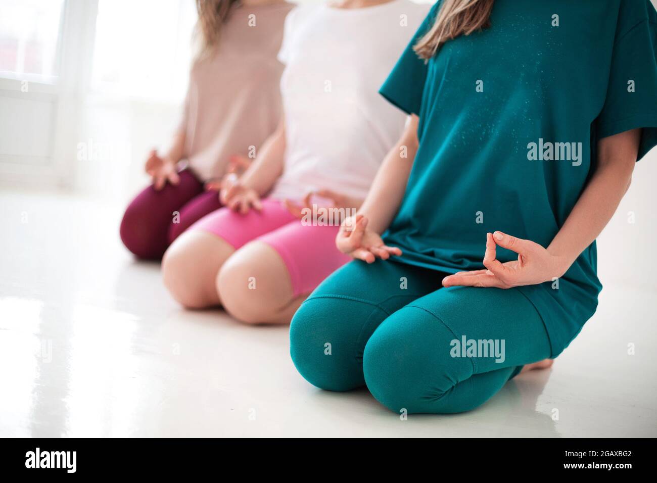 Drei junge, glückliche, gesunde Frauen in langen Sportbodysuits, die zusammen Yoga-Asanas während eines ziemlich meditativen Trainings oder einer Yoga-Gruppenklasse durchführen, isolieren sich Stockfoto