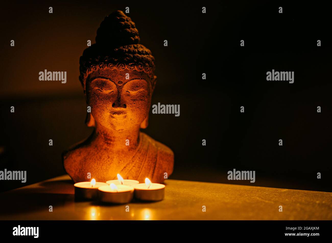 Buddha-Statue, die auf dem Tisch mit Teelicht-Kerzen ruht Stockfoto