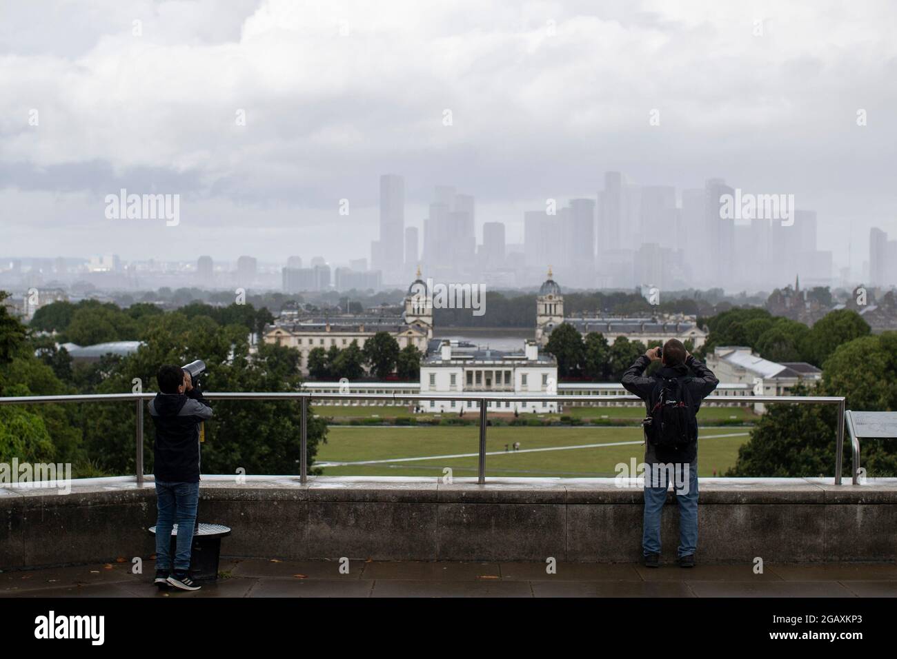 30/07/2021. London, Großbritannien. Ein Mitglied der Öffentlichkeit blickt während eines Regensturms im Greenwich Park im Südosten Londons auf Canary Wharf. Phot Stockfoto