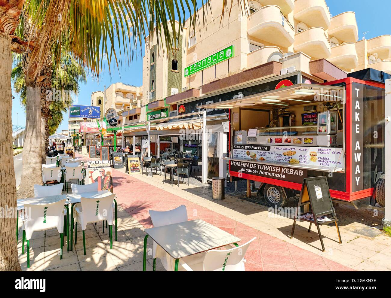 Orihuela, Spanien - 14. Mai 2021: Handelsstraße mit Restaurants und Cafés im Freien in der palmengesäumten Straße von Cabo Roig. Tourismus und Reisen, Stockfoto