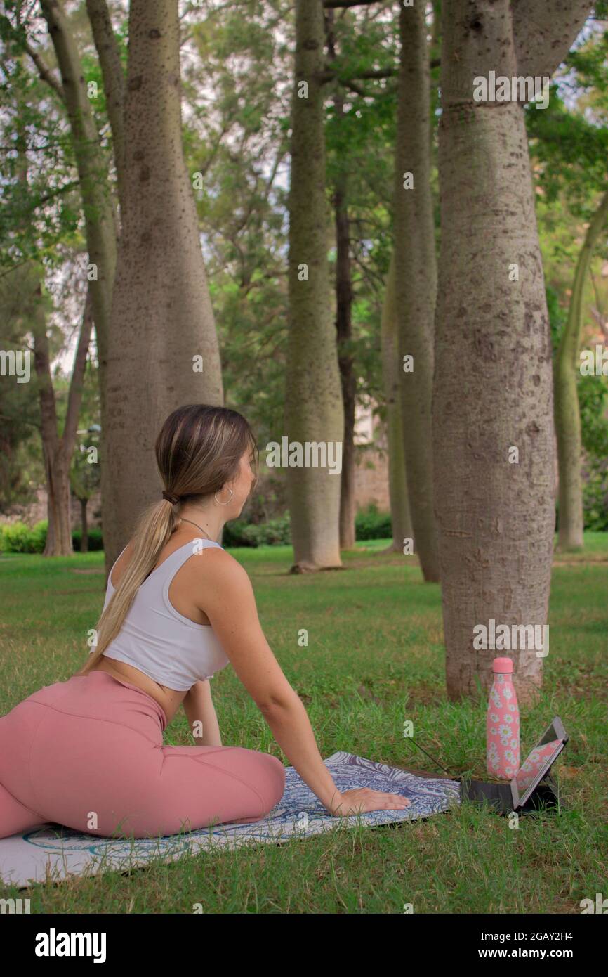 Vertikales Bild einer nicht erkennbaren jungen Frau, die sich vor dem Pilates-Kurs draußen im Stadtpark an einem sonnigen Sommertag ausdehnt. Pilates Outdoor 2021. Stockfoto