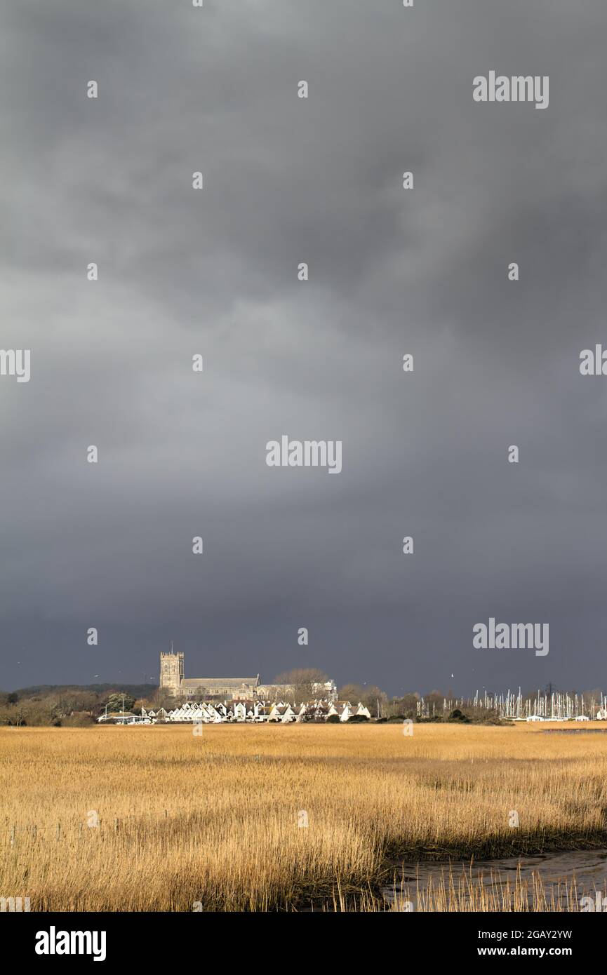 Christchurch Priory aus dem 15. Jahrhundert, von der Sonne gegen EINE Dunkler Stürmischer Himmel Über Den Schilfbetten Von Wick Hengistbury Head UK Stockfoto