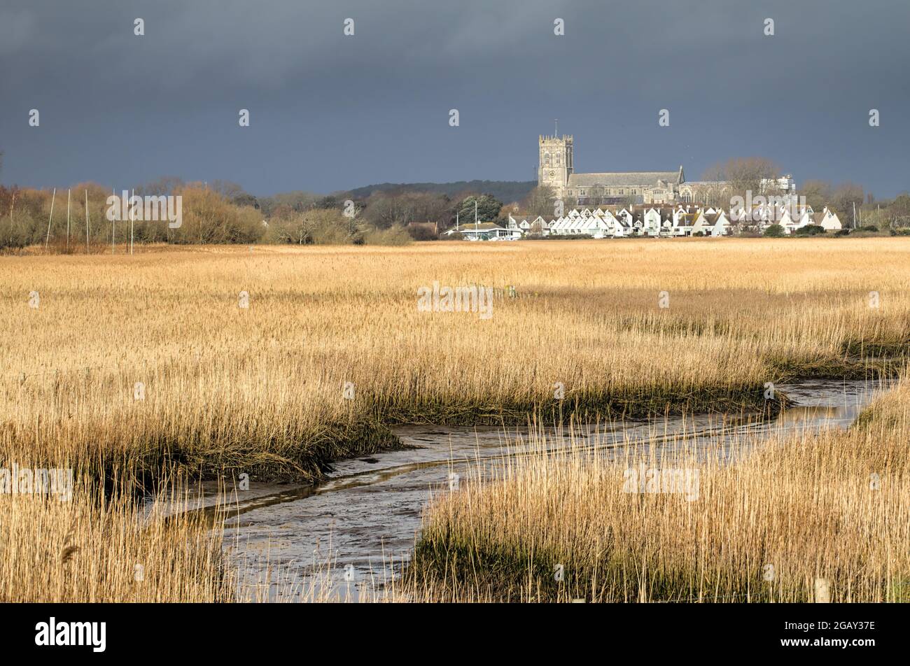 Christchurch Priory aus dem 15. Jahrhundert, von der Sonne gegen EINE Dunkler Stürmischer Himmel Über Den Schilfbetten Von Wick Hengistbury Head UK Stockfoto