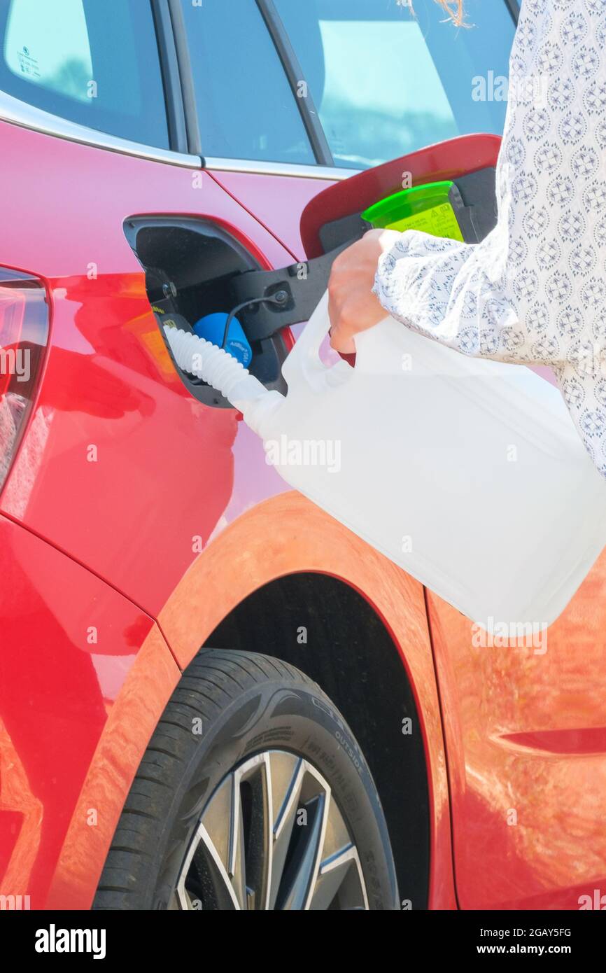 Frau, die eine Dieselmotorflüssigkeit aus dem Behälter in den Tank eines roten Autos auf dem Hintergrund von Windenergieanlagen einfüllt. Verringerung der Luftverschmutzung und Stockfoto