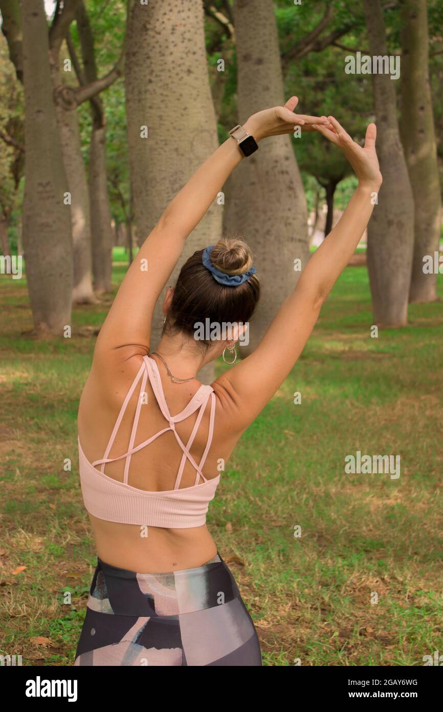 Vertikales Bild einer jungen Frau, die sich ausdehnt, um an einem sonnigen Sommertag im Stadtpark mit dem täglichen Pilates-Workout zu beginnen. Pilates Outdoor 2021. Stockfoto