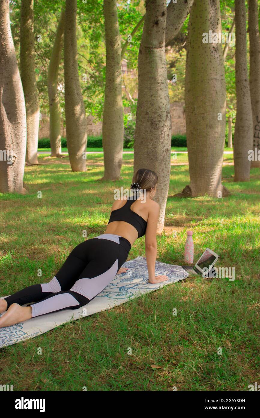 Vertikales Bild eines jungen Mädchens, das die Plankenpose macht, während sie sich im Sommer an einem sonnigen Tag im Stadtpark entspannt. Pilates Outdoor 2021. Stockfoto