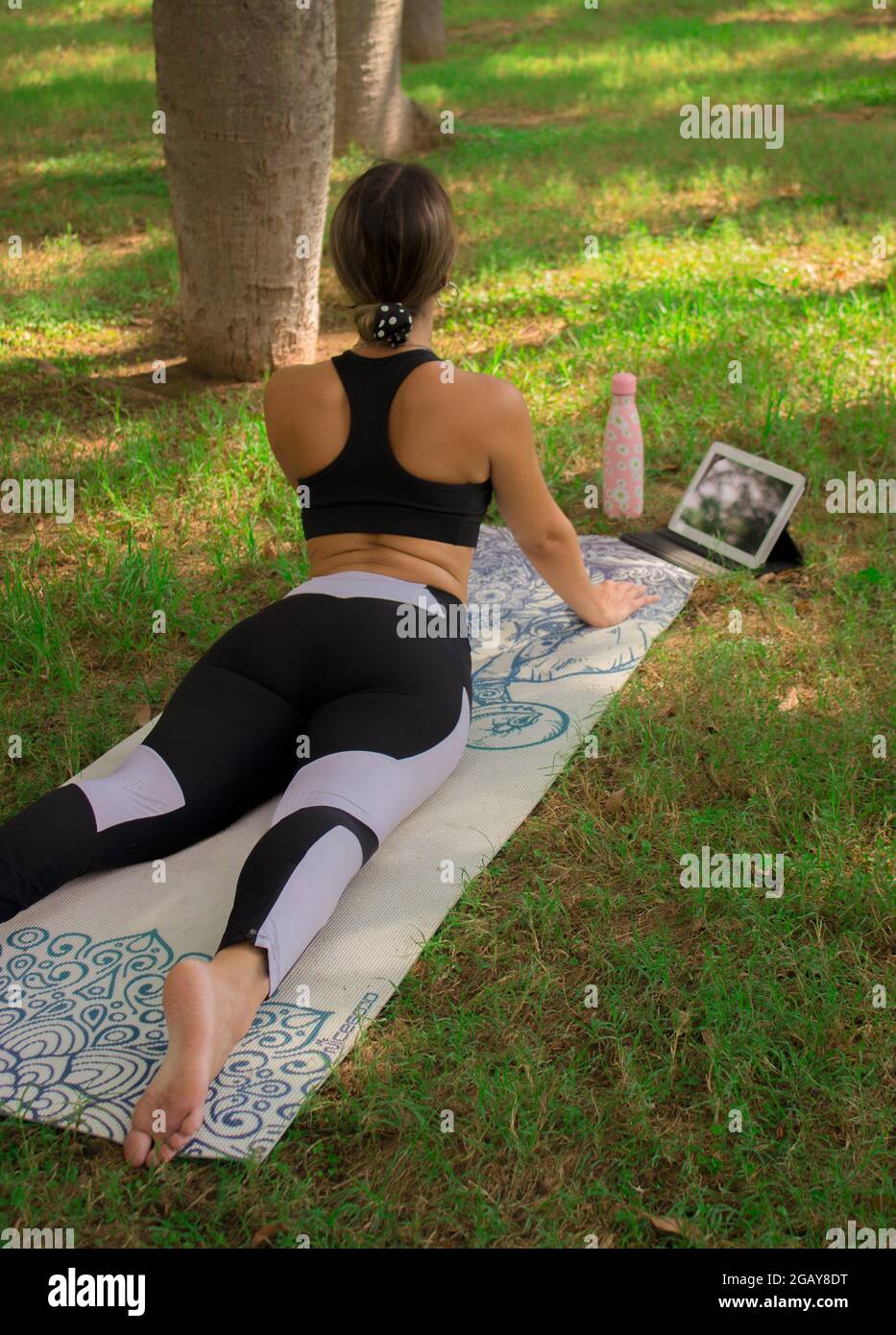Vertikales Bild eines jungen Mädchens, das die Kobra-Pose macht, während sie sich an einem sonnigen Sommertag im Stadtpark entspannt. Pilates 2021 Stockfoto