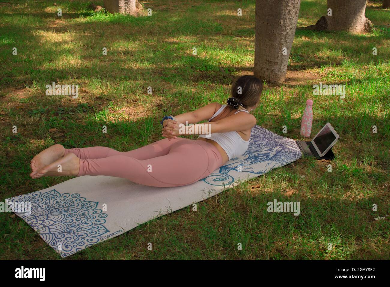 Junge Frau, die an einem sonnigen Sommertag im Stadtpark entspannt, in Heuschreckenpose. Pilates Outdoor 2021. Stockfoto