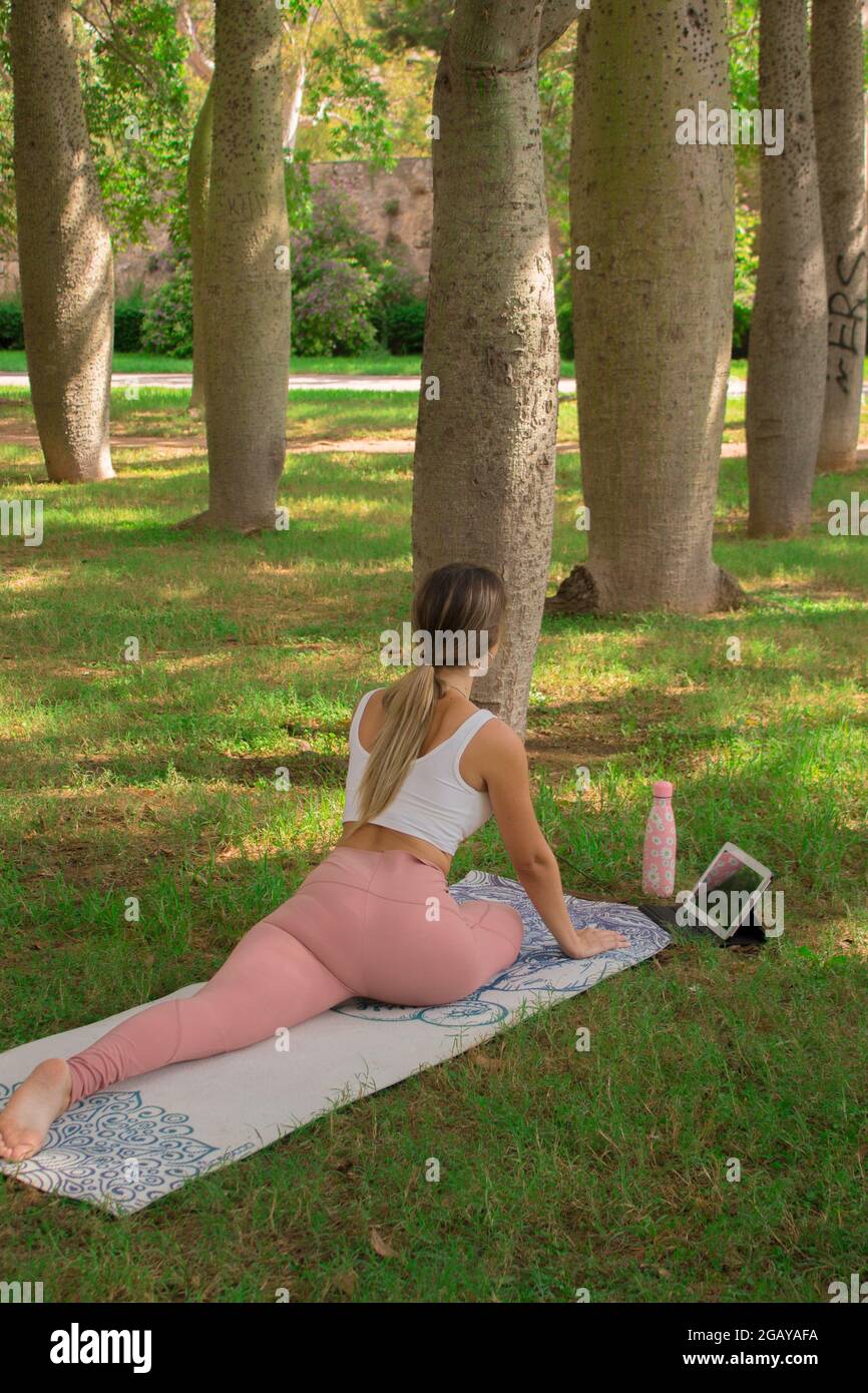 Vertikales Bild einer nicht erkennbaren jungen Frau, die sich vor dem Pilates-Kurs im Stadtpark an einem sonnigen Tag im Sommer ausdehnt. Pilates Outdoor 2021. Stockfoto
