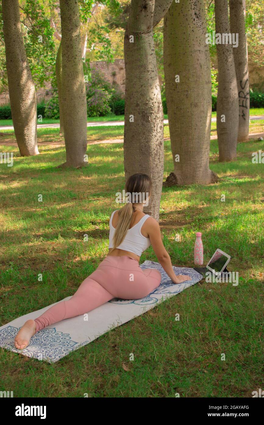 Vertikales Bild einer nicht erkennbaren jungen Frau, die sich vor dem Pilates-Kurs im Stadtpark an einem sonnigen Tag im Sommer ausdehnt. Pilates Outdoor 2021. Stockfoto