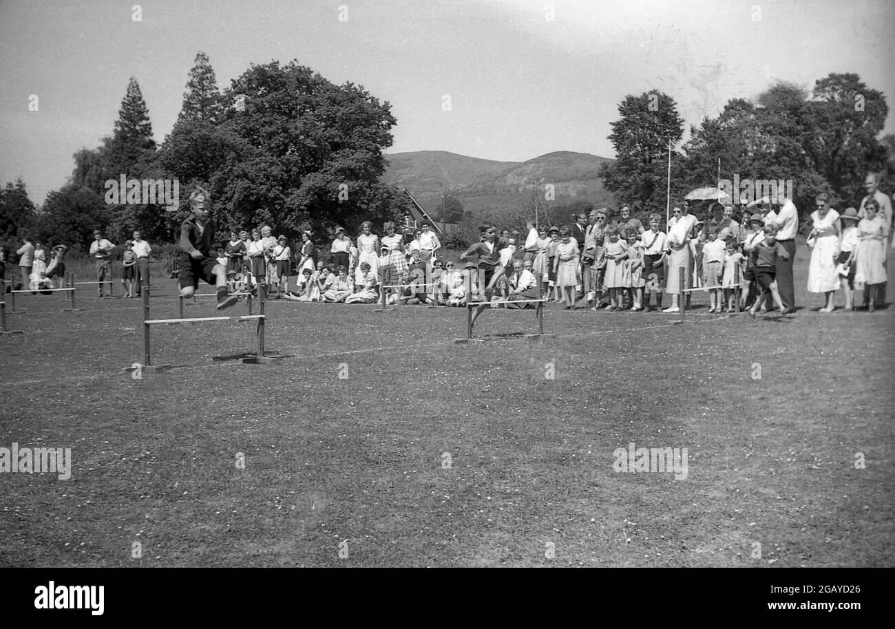 60er Jahre, historisch, Schulsport, draußen auf einem Grasfeld, junge Jungen machen ein Hürdenrennen, springen über kleine Holzzäune, beobachtet von Eltern und anderen Kindern, England, Großbritannien. Stockfoto