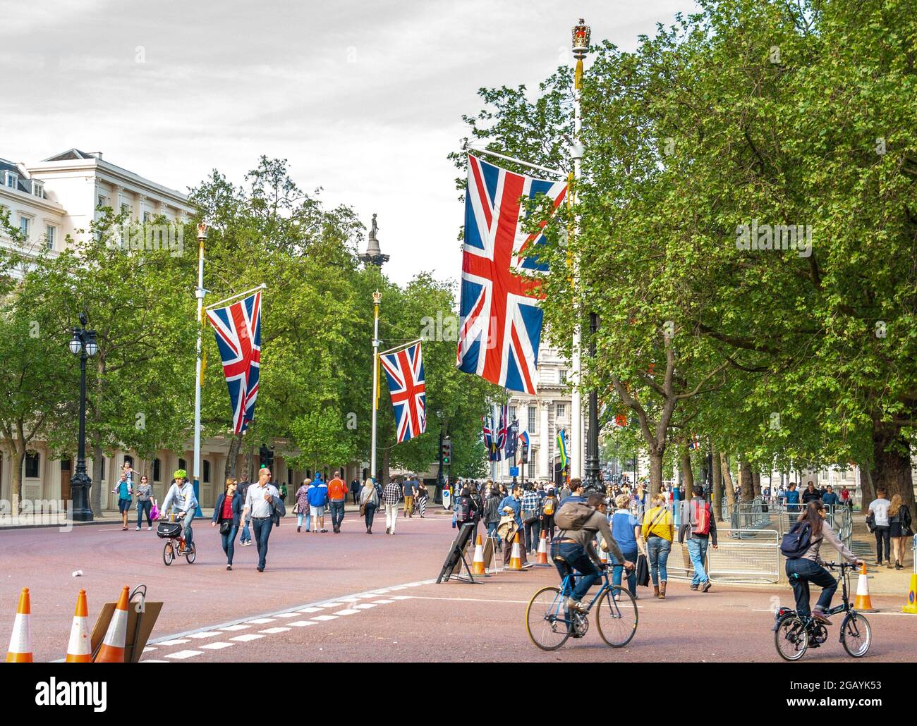 London - UK, 2015-05-10: Londen feiert den 70. Jahrestag des Endes des Zweiten Weltkriegs in Europa am VEday, dem Gedenken an den Tag des Sieges in Europa. Die Menschen schlendern und radeln die Mall entlang, eine von Bäumen gesäumte königliche Straße, die vom Trafalgar Square zum Buckingham Palace führt und auf beiden Seiten mit britischen Flaggen geschmückt ist. Hier mit Blick auf den Trafalgar Square. Im Hintergrund erhebt sich die Statue von Admiral Horatio Nelson auf der Nelson-Säule knapp über den Bäumen. Foto archivieren. Stockfoto
