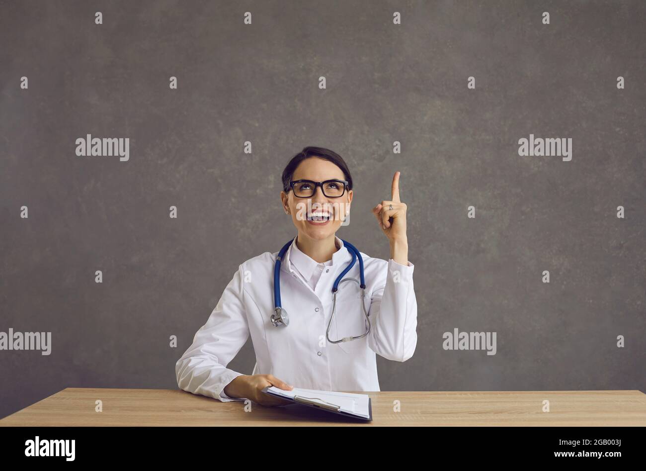 Glückliche junge Ärztin, die von einer coolen Idee getroffen wurde, lächelte und zeigte ihren Finger nach oben Stockfoto