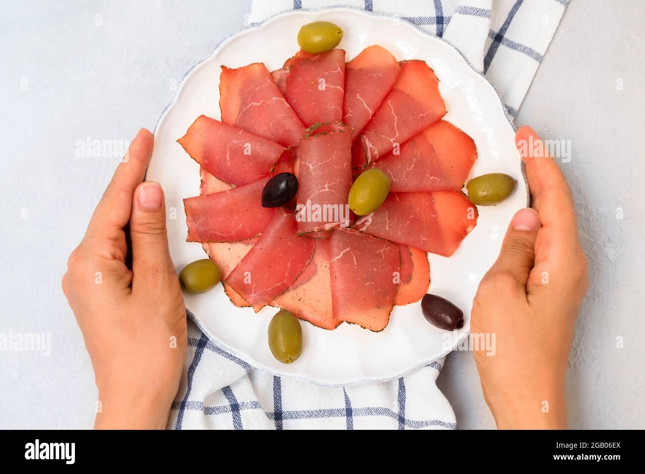Ansicht der Hände mit weißem Teller und Rippenscheiben von Pastrami (getrocknetes Fleisch aus dem balkan), verziert mit Oliven Stockfoto