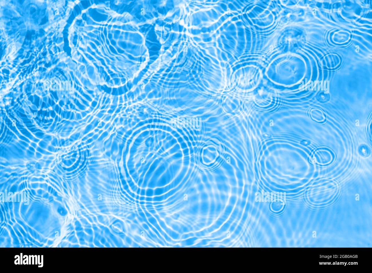 Oberfläche von hellblauem transparentem Wasser aus dem Schwimmbad mit Kreisen auf dem Wasser. Trendige abstrakte Natur Hintergrund. Wasser Wellen im Sonnenlicht Stockfoto