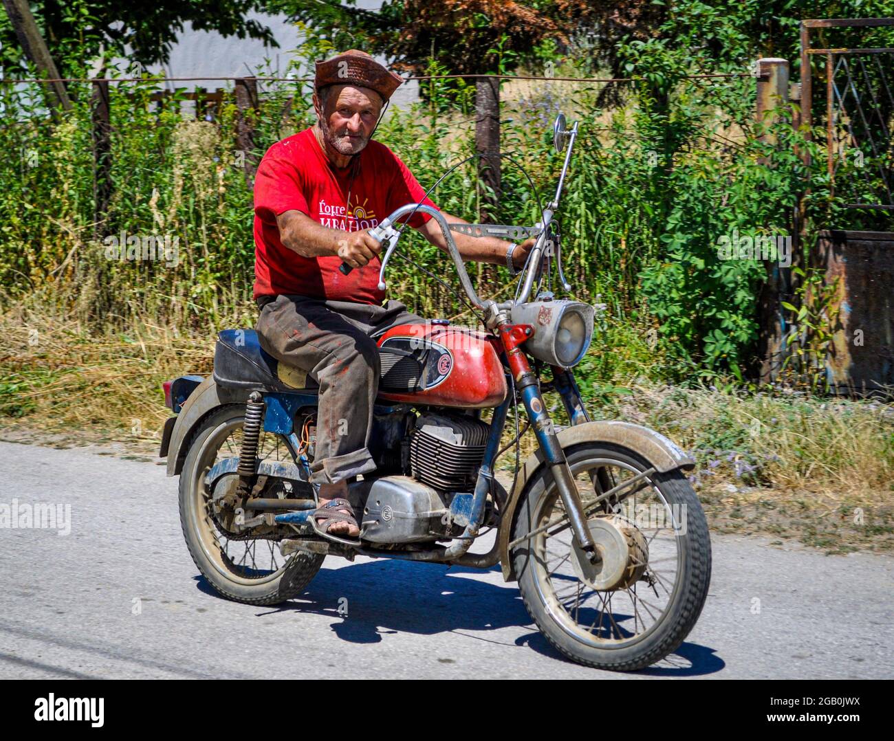 Motorradfahrer mit Hut auf einem alten Motorrad auf einer Landstraße Stockfoto