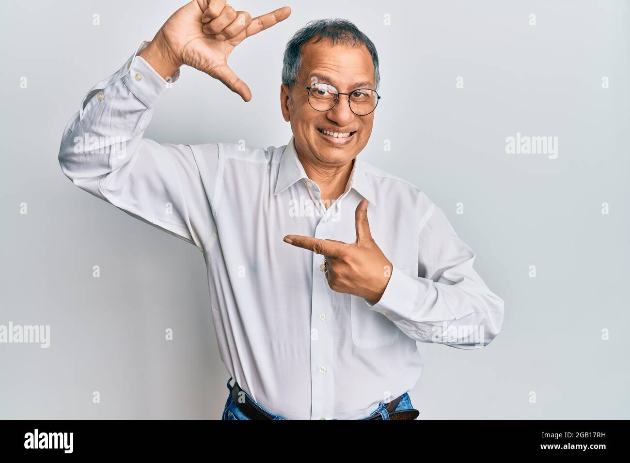 Mittelalter indischer Mann trägt lässige Kleidung und Brille lächelnd machen Rahmen mit Händen und Fingern mit glücklichen Gesicht. Kreativität und Fotografie conce Stockfoto