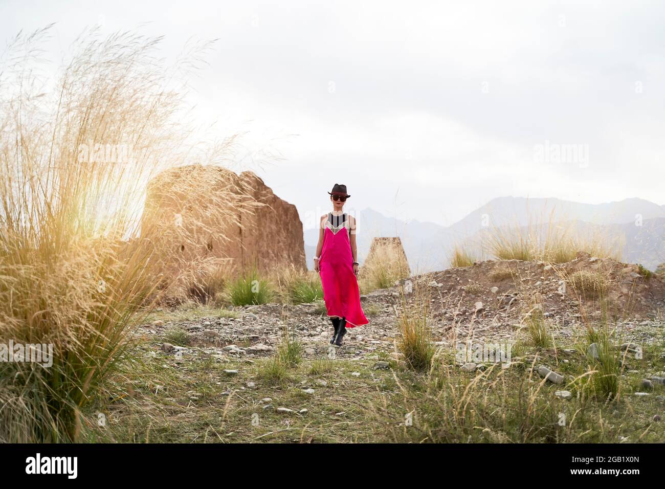 asiatische Frau in rotem Kleid, die in der Morgensonne an einem verlassenen historischen Ort spazieren geht Stockfoto