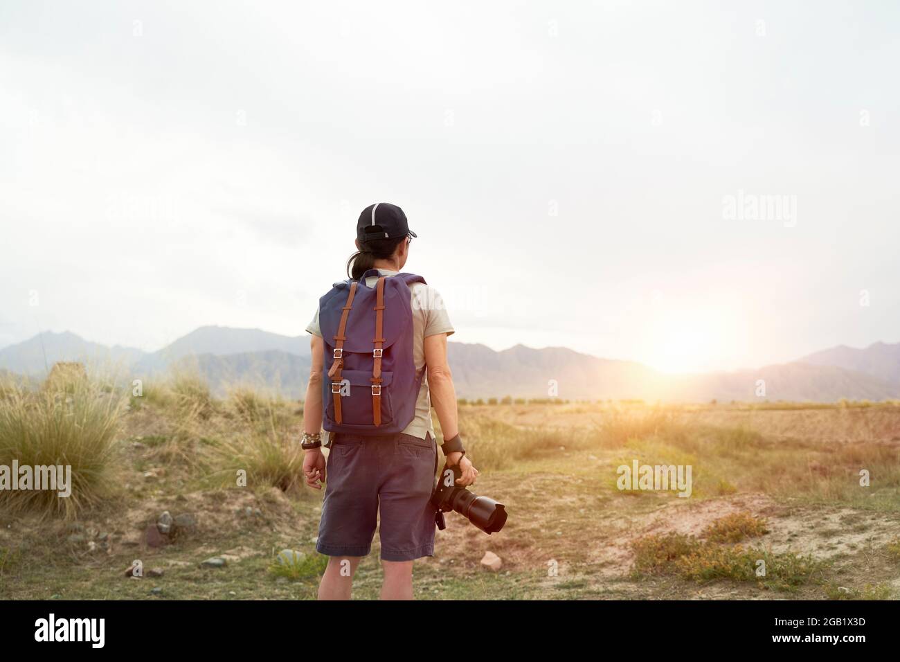 Rückansicht eines asiatischen Fotografen, der im Morgenlicht mit der Kamera in der Hand die Sicht betrachtet Stockfoto