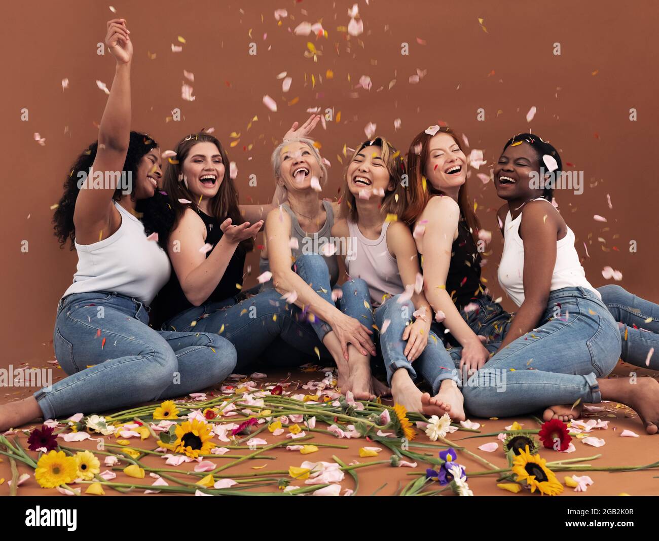 Eine multiethnische Gruppe glücklicher Frauen, die unter fallenden Blütenblättern sitzen Stockfoto