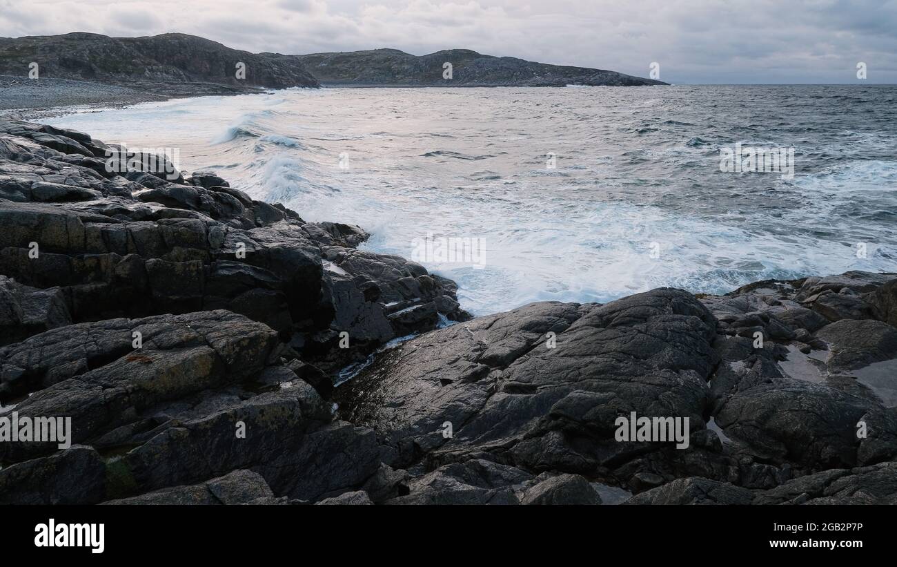 Weiße Schaumwellen laufen an der felsigen Küste des weißen Meeres.dramatischer Himmel, epische Meereslandschaft. Ein Sturm auf See. Sturmwellen. Nordisch, Barentssee, Meer. Stockfoto