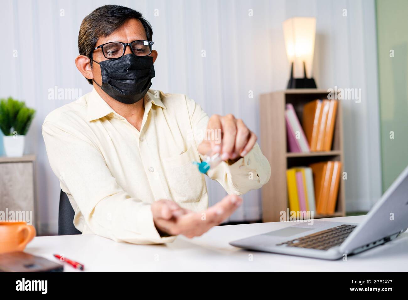 Geschäftsmann im Büro mit medizinischer Maske mit Handdesinfektionsmittel vor Arbeitsbeginn - Konzept der Büro wieder öffnen, neue normale und Coronavirus covid-19 Stockfoto