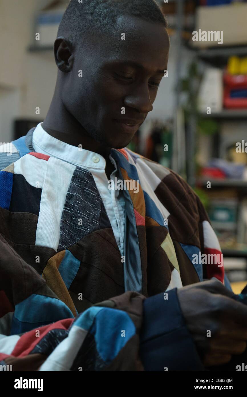 Afrikanischer Mann in traditioneller, farbenfroher Kleidung in einer Nähwerkstatt. Stockfoto