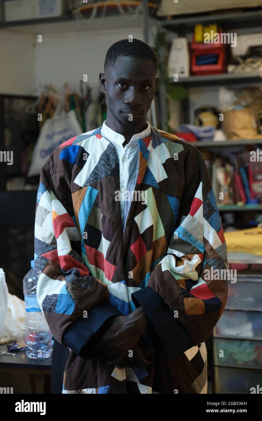 Afrikanischer Mann in traditioneller, farbenfroher Kleidung und Hut in seiner Nähwerkstatt. Stockfoto
