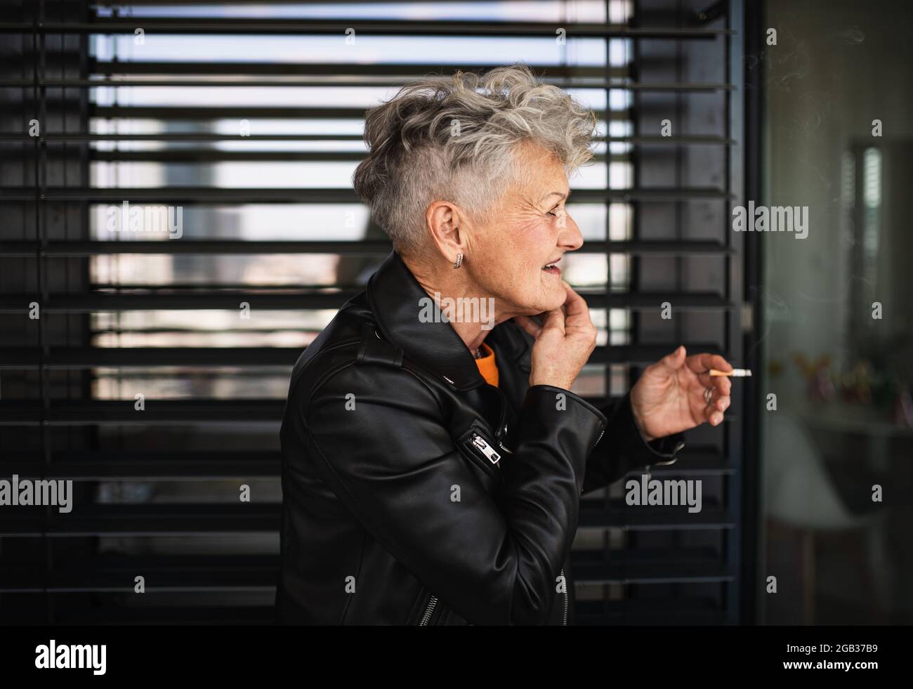 Porträt einer älteren Frau mit einer Zigarette, die auf schwarzem Hintergrund steht und sich entspannt. Stockfoto