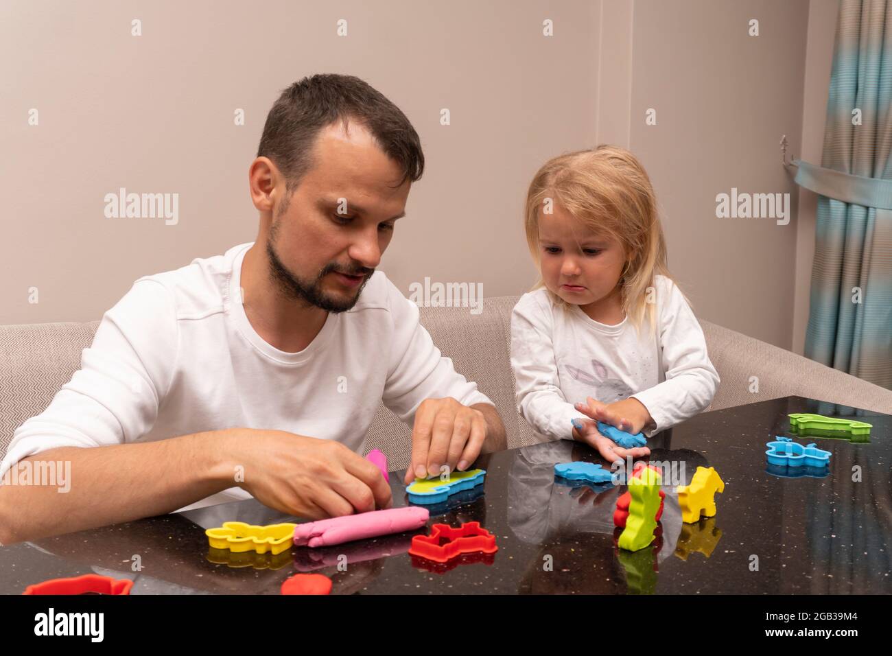 Weinendes kleines Kind und junger kaukasischer Vater spielen mit bunt Teig spielen Stockfoto