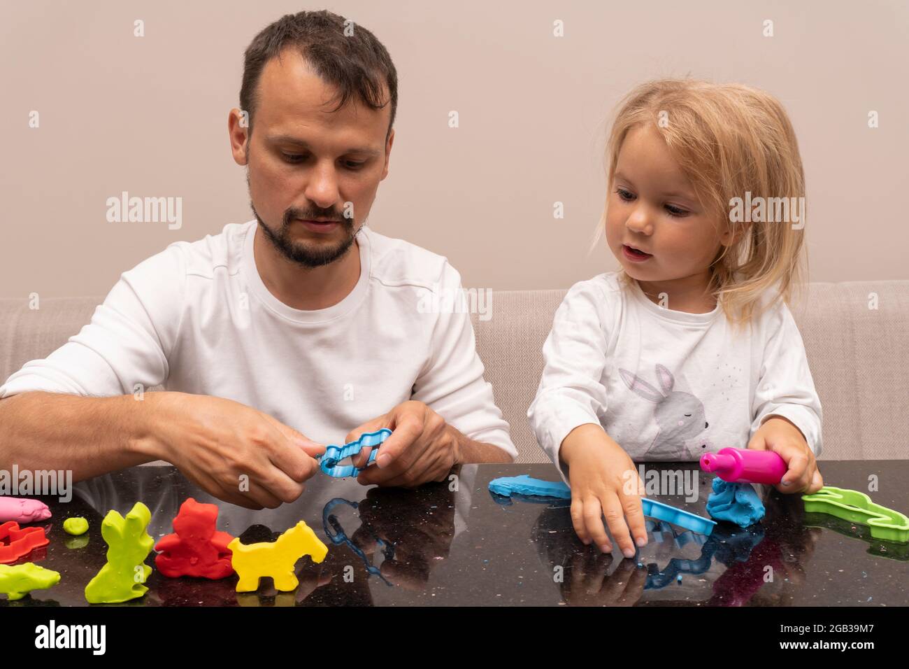 Der junge Kaukasusmann spielt mit der Tochter, die bunte Tiere aus macht Spielteig Stockfoto