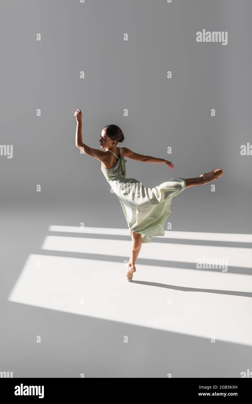 Ballerina tanzt und steht auf einem Bein auf grauem Hintergrund mit Sonnenlicht Stockfoto